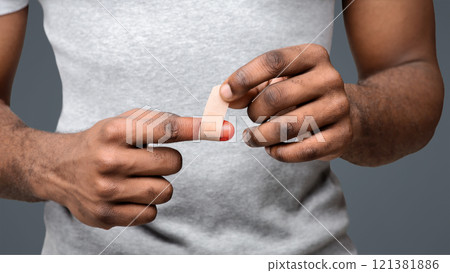Black man using adhesive tape on injured finger, self-treatment after trauma, close up 121381886