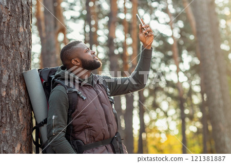 Black guy with backpack holding smartphone up, looking for gps in woods, got lost 121381887
