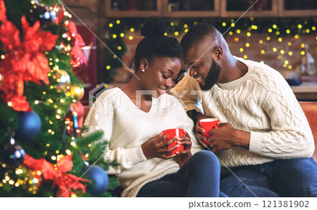 Celebrating Christmas together. Young african couple holding red mugs, reading coffee grounds to learn their fortune, enjoying holidays together. 121381902