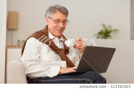 Retired Life. Happy Senior Gentleman Using Laptop Watching Film Having Coffee Sitting On Sofa Indoor. Selective Focus Retired Life. Happy Senior Gentleman Using Laptop Watching Film Having Coffee Sitting On Sofa Indoor. Selective Focus 121381925