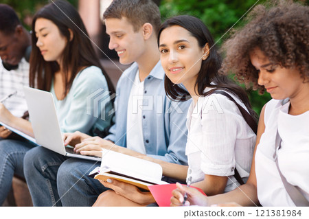 Exams Preparation. Group Of Multi-Ethnic Students Studying Together Outdoors, Selective Focus On Arabic Girl With Notepad 121381984