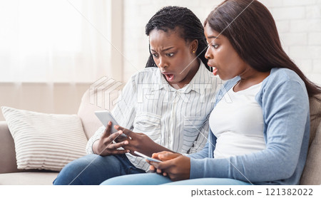 Shock content. Two dazed black girlfriends looking at smartphone screen with mouth open, can not believe their eyes, free space 121382022