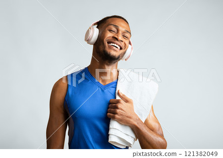 Active Lifestyle. Portrait of smiling afro guy with towel on his shoulder listening to music in headphones, yellow wall Active Lifestyle. Portrait of smiling afro guy with towel on his shoulder listening to music in headphones, yellow wall 121382049