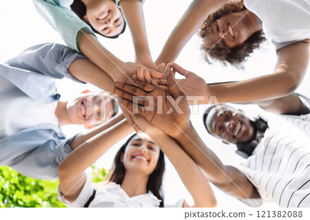 Friends Unity. Low Angle Portrait Of Happy Teenage People Stacking Hands Together And Smiling At Camera, Showing Teamwork And Cooperation Friends Unity. Low Angle Portrait Of Happy Teenage People Stacking Hands Together And Smiling At Camera, Showing Teamwork And Cooperation 121382088