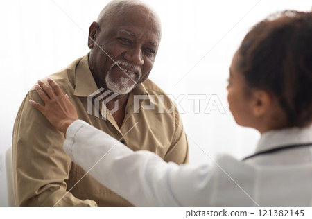 Support Concept. Closeup of black female doctor tapping patting patient's shoulder for empathy and encouragement during appointment in clinic. General practitioner cheering mature man at office Support Concept. Closeup of black female doctor tapping patting patient's shoulder for empathy and encouragement during appointment in clinic. General practitioner cheering mature man at office 121382145