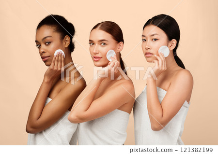 Facial Skincare. Three Multiethnic Women Using Cotton Pads Posing In Bath Towels Over White Background. Studio Shot 121382199