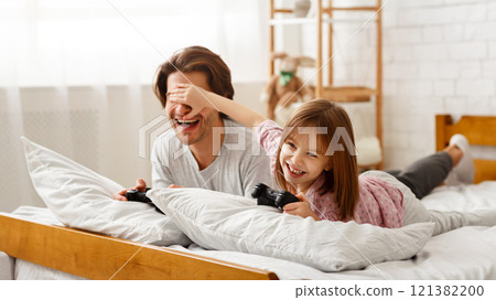 Playful kid girl covering her dad eyes while playing videogame, cheating to win, free space Playful kid girl covering her dad eyes while playing videogame, cheating to win, free space 121382200