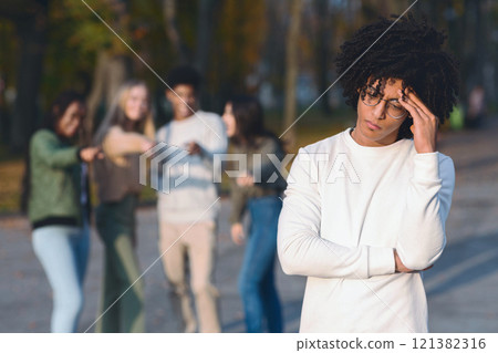 Multiracial group of teenagers pointing at frustrated black guy, spending time in park Multiracial group of teenagers pointing at frustrated black guy, spending time in park 121382316