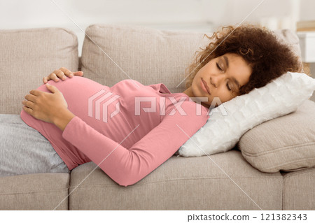 Tranquil pregnant woman sleeping on back and embracing belly, lying on sofa 121382343