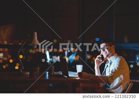 Successful Businessman Talking On Phone Working Sitting Near Window In Modern Office At Night. Copy Space Successful Businessman Talking On Phone Working Sitting Near Window In Modern Office At Night. Copy Space 121382350