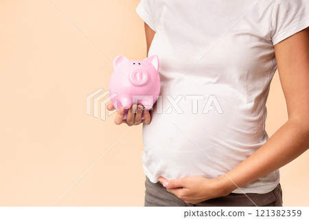 Pregnancy And Budget. Unrecognizable Pregnant Woman Holding Piggybank Standing Over White Studio Background. Cropped 121382359