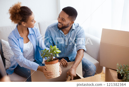 Cheerful Afro Husband And Wife Packing Moving Boxes Together Sitting On Couch Indoor. Selective Focus 121382364