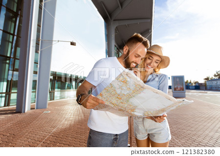 Young couple standing in front of airport terminal building, looking at map, empty space Young couple standing in front of airport terminal building, looking at map, empty space 121382380