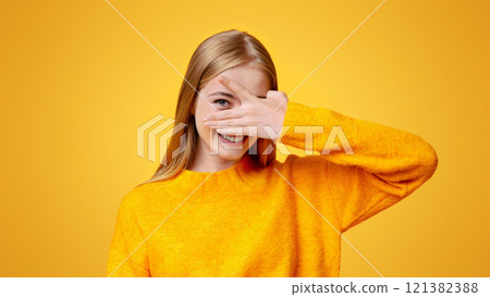 Playful teen girl covering face with hand and peeking through fingers over orange background with copy space Playful teen girl covering face with hand and peeking through fingers over orange background with copy space 121382388