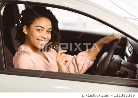 Joyful Afro Woman Showing Car Key Smiling To Camera Sitting In Driver's Seat In New Automobile Dealership Store. Selective Focus Joyful Afro Woman Showing Car Key Smiling To Camera Sitting In Driver's Seat In New Automobile Dealership Store. Selective Focus 121382389