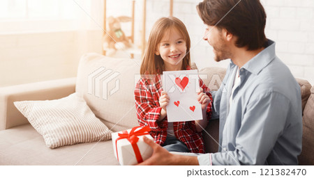 Daddy and daughter celebrating Father Day together at home, little girl holding self made card, dad carrying gift box Daddy and daughter celebrating Father Day together at home, little girl holding self made card, dad carrying gift box 121382470