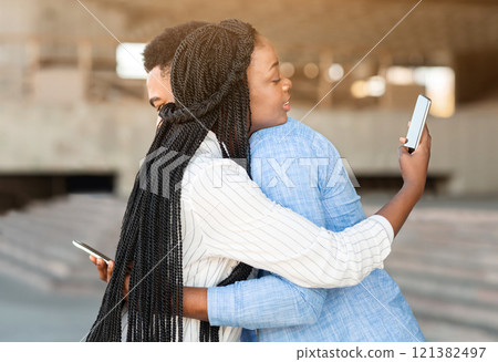 Smartphone addiction concept. Young man and woman hugging each other, but looking at mobile phones over shoulder. 121382497