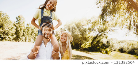 Family walk. Parents play with his daughters outdoors, girl sitting on father shoulders 121382504