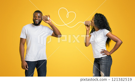 Attractive black girl in love talking by can phone with her boyfriend, love is in the air, yellow studio background, empty space 121382519