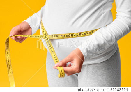 Unrecognizable Pregnant Lady Measuring Belly With Tape Standing Over Pink Studio Background. Cropped, Selective Focus 121382524