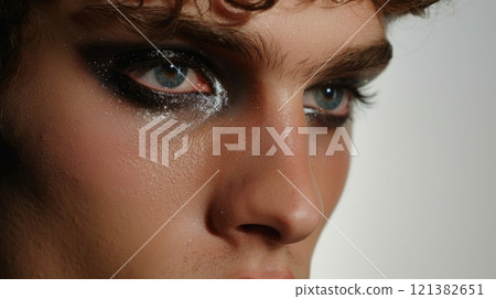 A man's face, with heavy black eyeliner and eyeshadow, stares off to the side. A man's face, with heavy black eyeliner and eyeshadow, stares off to the side. 121382651