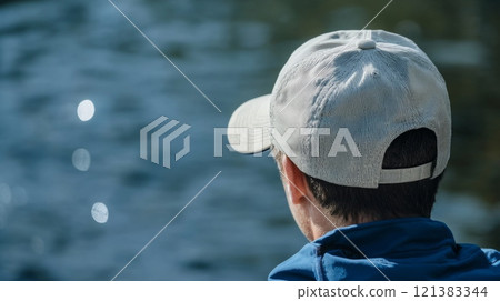 A person sits quietly by the water's edge, gazing out at the shimmering lake and reflecting on nature's beauty. 121383344