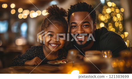 A young girl and her father smile brightly as they enjoy a special dessert together in a warmly lit restaurant filled with holiday decorations. 121383699