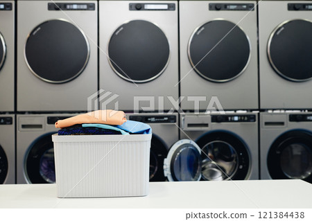 Background shot of basket full of colored clothes on folding table in self service laundry with professional dryers and washing machines, copy space Background shot of basket full of colored clothes on folding table in self service laundry with professional dryers and washing machines, copy space 121384438