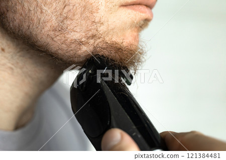 A man trims his beard with a trimmer. An electric razor trimming a beard. A man trims his beard with a trimmer. An electric razor trimming a beard. 121384481