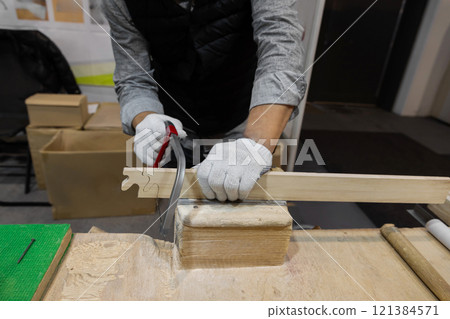 male hands in work gloves sawing wooden blank with thin hand saw 121384571