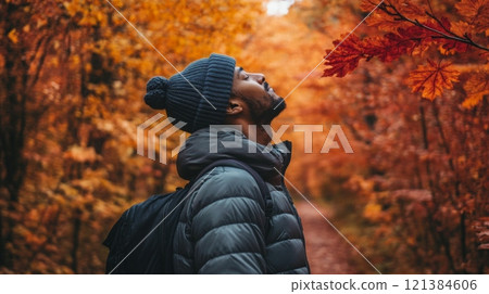 A man enjoys the beauty of autumn as he gazes up at colorful leaves in a tranquil forest. The vibrant hues of orange and red surround him, creating a perfect backdrop for reflection and appreciation. A man enjoys the beauty of autumn as he gazes up at colorful leaves in a tranquil forest. The vibrant hues of orange and red surround him, creating a perfect backdrop for reflection and appreciation. 121384606