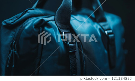 A black backpack is highlighted in low light, emphasizing the texture of the fabric and the design of the straps. The dark setting adds an intriguing contrast, enhancing its features. 121384853