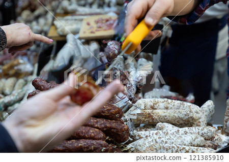 Seller cuts a slice of meat and gives it taste to woman Seller cuts a slice of meat and gives it taste to woman 121385910