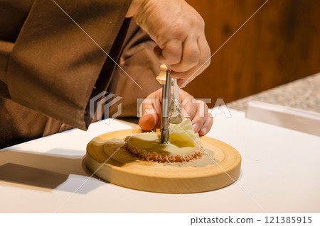 middle section of a middle aged man with hands in monk's robe cutting cheese 121385915