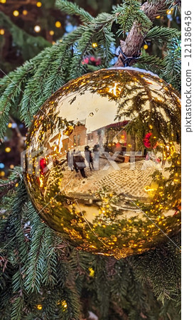 Shiny golden Christmas ornament reflecting festive market scene, surrounded by snow-covered evergreen branches and warm lights Shiny golden Christmas ornament reflecting festive market scene, surrounded by snow-covered evergreen branches and warm lights 121386436
