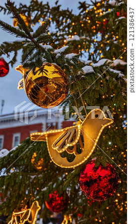 Christmas tree branch decorated with glowing golden bird ornament, reflective golden ball, and shiny red baubles, close up Christmas tree branch decorated with glowing golden bird ornament, reflective golden ball, and shiny red baubles, close up 121386437