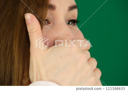 Surprised caucasian girl covering her mouth and looking at camera isolated over green background 121386633