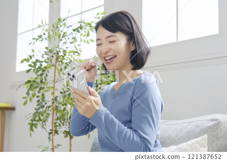 Middle-aged woman holding a smartphone, fist pump, living room 121387652
