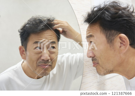 A man in his 50s looking in the mirror and worrying about his gray hair A man in his 50s looking in the mirror and worrying about his gray hair 121387666