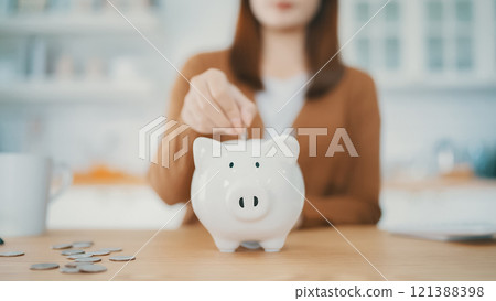 Young Asian woman putting coin in piggy bank. Save money and financial investment 121388398
