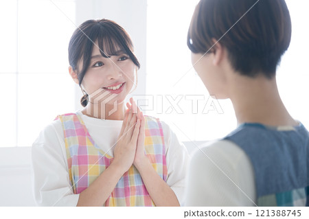 Close-up of two women, such as housewives and nursery teachers, wearing aprons, talking and communicating. Close-up of two women, such as housewives and nursery teachers, wearing aprons, talking and communicating. 121388745