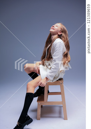 A Joyful Girl Posing Gracefully on a High Stool, Wearing a Stylish Outfit with Confidence 121389659