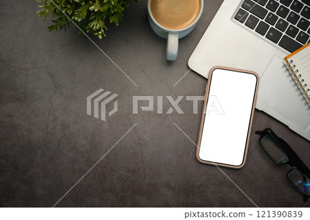 Top view of modern workspace with smartphone, laptop, coffee cup and notebook on dark textured surface 121390839