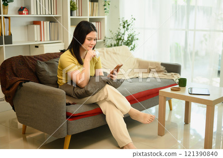 Happy young woman in casual clothing relaxing on a couch and using her mobile phone 121390840