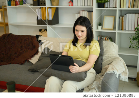 Young happy caucasian woman using digital tablet sitting on the sofa at home. Young happy caucasian woman using digital tablet sitting on the sofa at home. 121390893