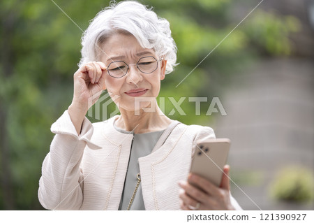 Senior woman squinting her eyes and looking at her smartphone screen Senior woman squinting her eyes and looking at her smartphone screen 121390927