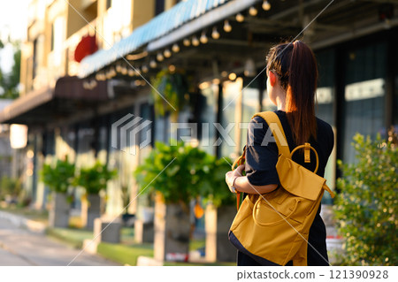 Young woman tourist with yellow backpack walking through a city street at daytime Young woman tourist with yellow backpack walking through a city street at daytime 121390928