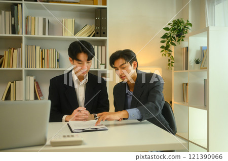 Two businessmen in formal suit reviewing a contract or report together in modern office 121390966