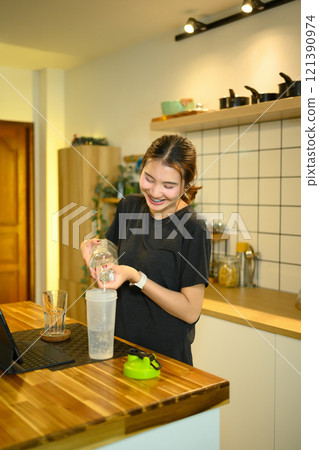 Young asian woman preparing protein shake after workout in a home kitchen Young asian woman preparing protein shake after workout in a home kitchen 121390974