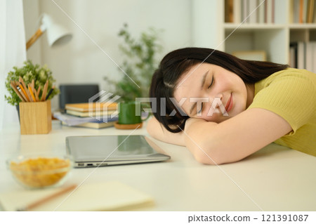 Young woman sleeping on a desk in front of her laptop taking break during online learning 121391087
